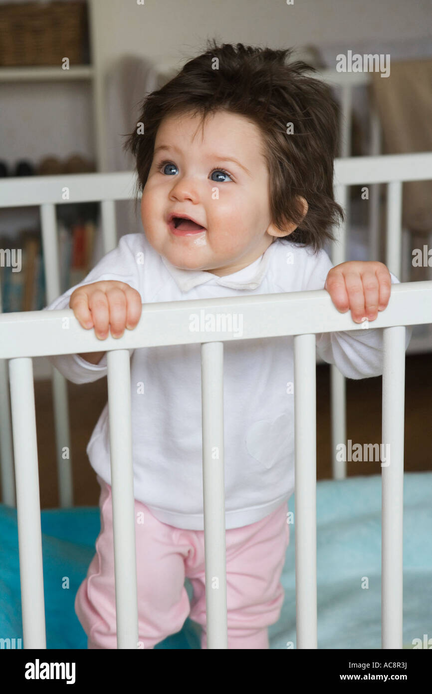 Baby girl standing in a crib Stock Photo Alamy