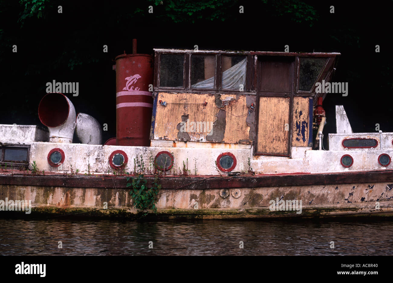 Dilapidated small ship covered in growth, rust and peeling paint on the River Thames at Hampton, England Stock Photo