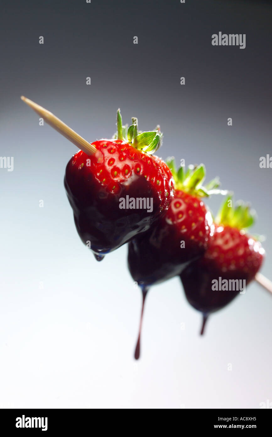 Three strawberries on a kebab skewer dipped in chocolate fountain Stock