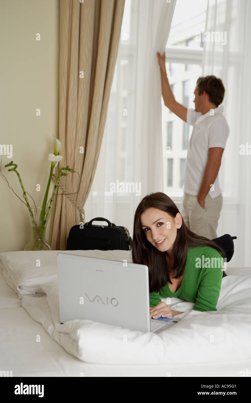 woman lying on bed with laptop, man standing at the window Stock Photo