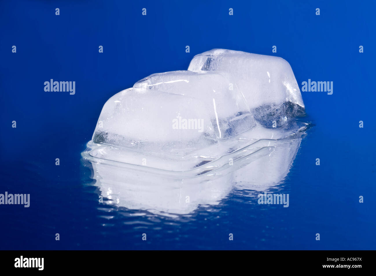 Melting ice cube with water drops on a mirror - blue background Stock ...