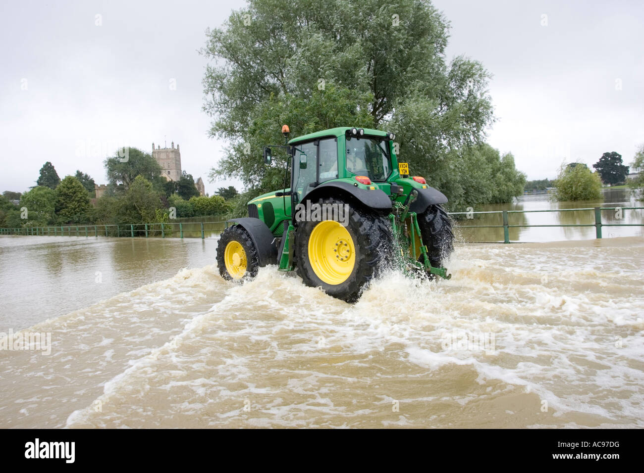 Green tractor driving along flooded road opposite Tewkesbury Abbey Gloucestershire UK Stock Photo