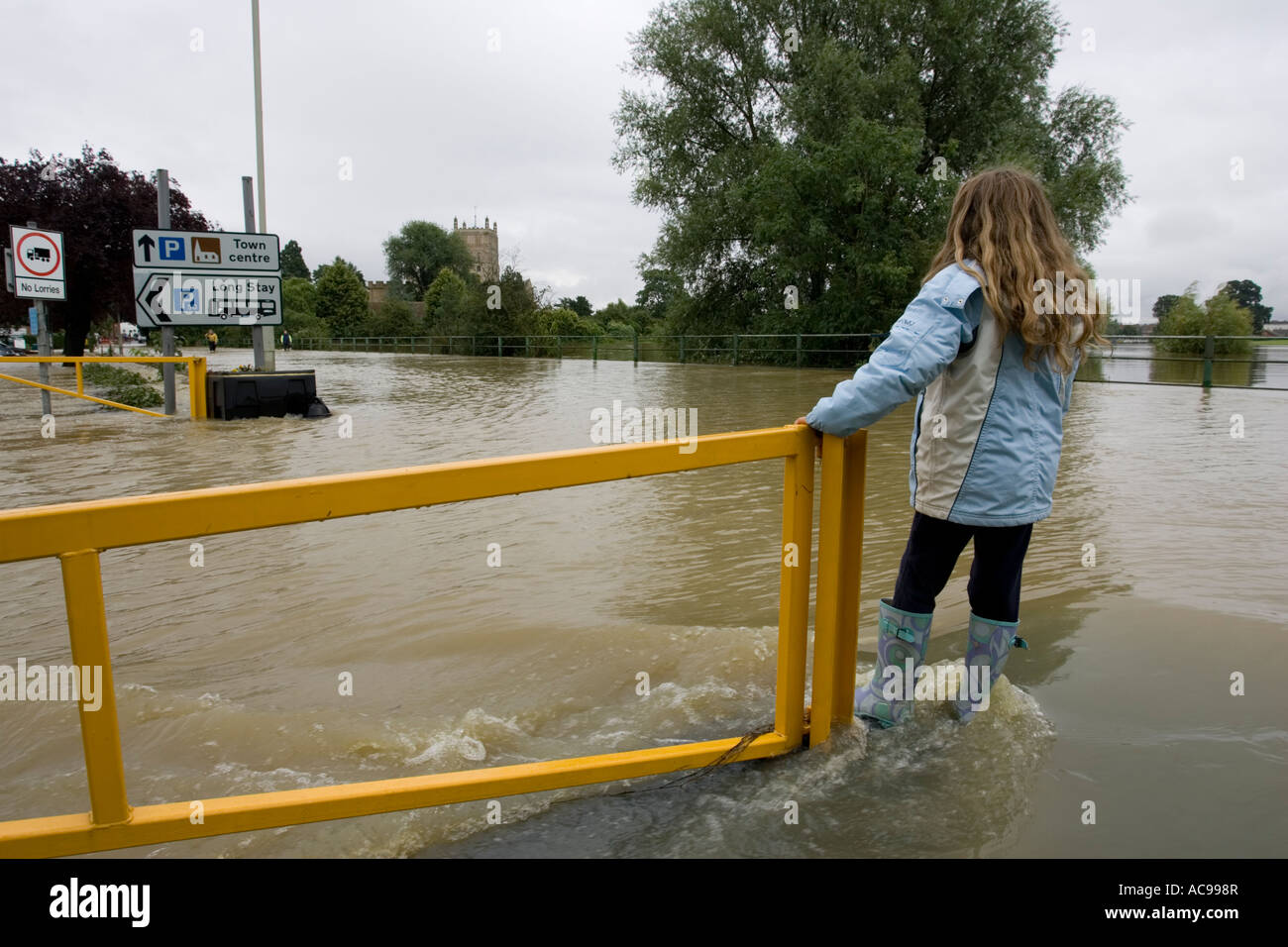 Young girl standing on flooded road opposite Tewkesbury Abbey Gloucestershire UK Stock Photo