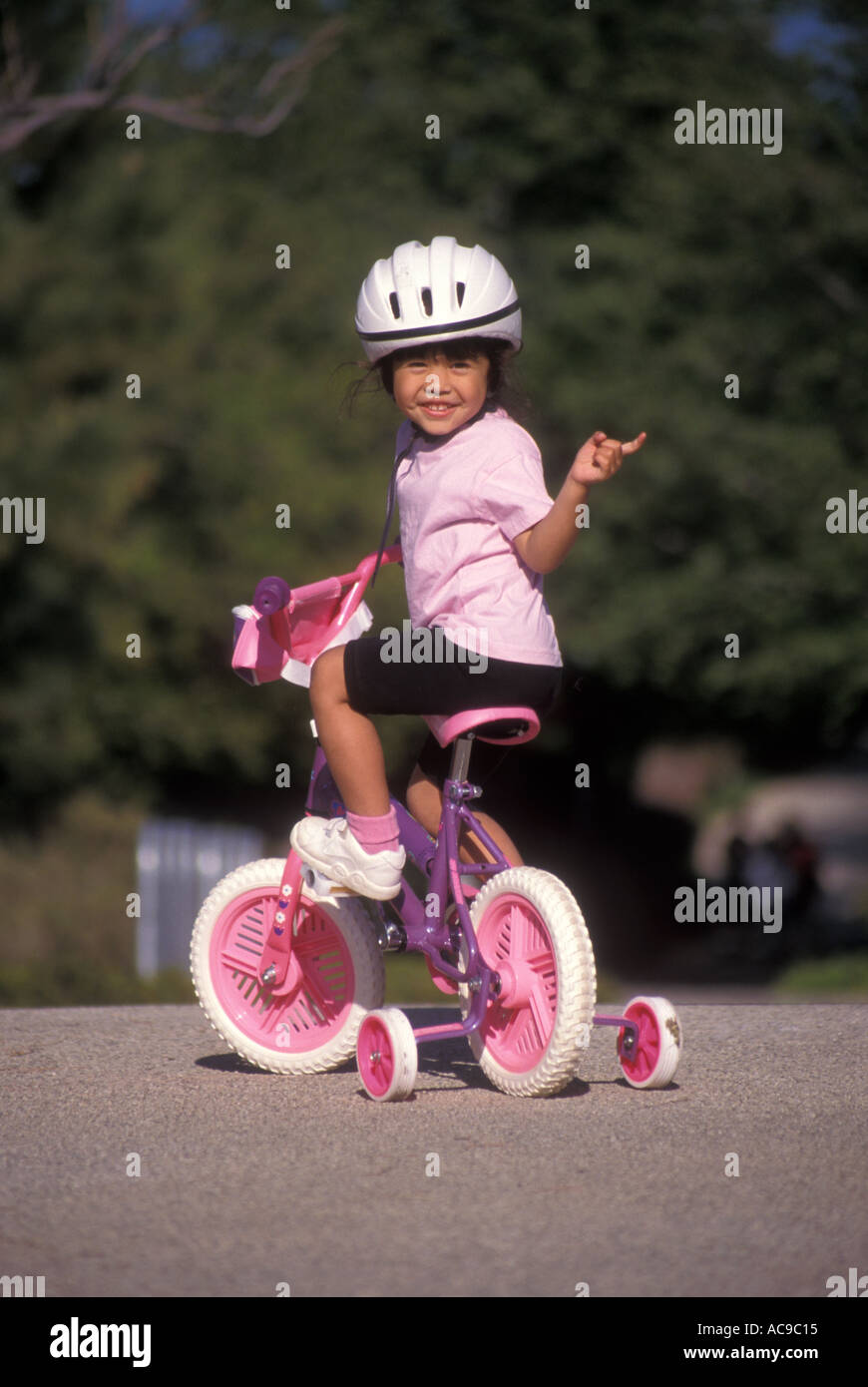 Children child  bicycle bike with training wheels Filipina toddler girl smiling wearing a helmet turning around to wave  POV MR ©Myrleen Pearson Stock Photo