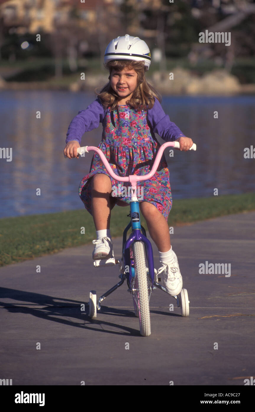little girl 4-5 year years old riding bicycle with training wheels near a lake bicycles bike bikes training wheels outdoor activity MR © Stock Photo