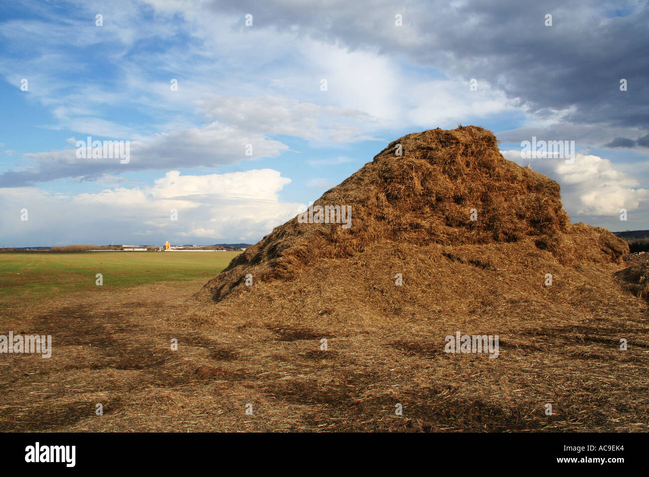 Large haystack under a wide open sky with distant industrial buildings ...