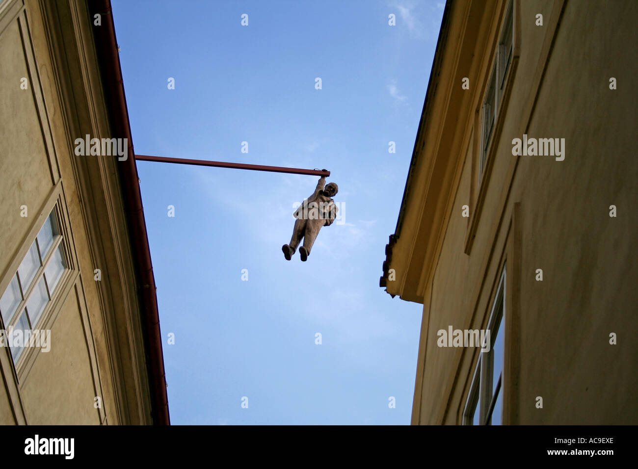 Statue of Sigmund Freud hanging by one hand from a pole between buildings against a clear sky in Prague. Stock Photo