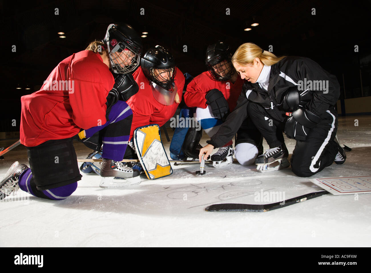 Women hockey players on ice looking at game plan with coach Stock Photo