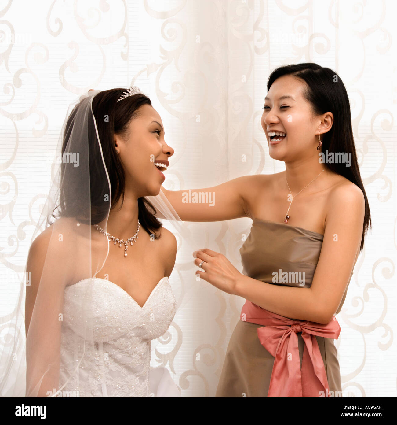 Asian bridesmaid laughing with African American bride Stock Photo
