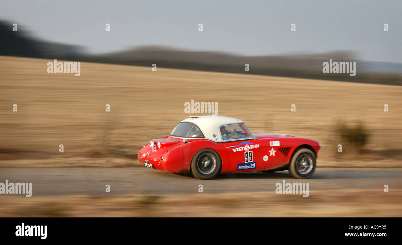 Side view of Red Austin Healey 100/6 rally car at full speed on tarmac countryside road Stock Photo