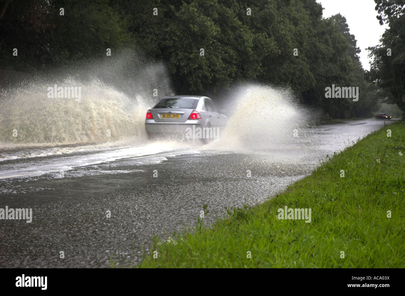 Car driving through flooded road spraying water after heavy rain Stock Photo