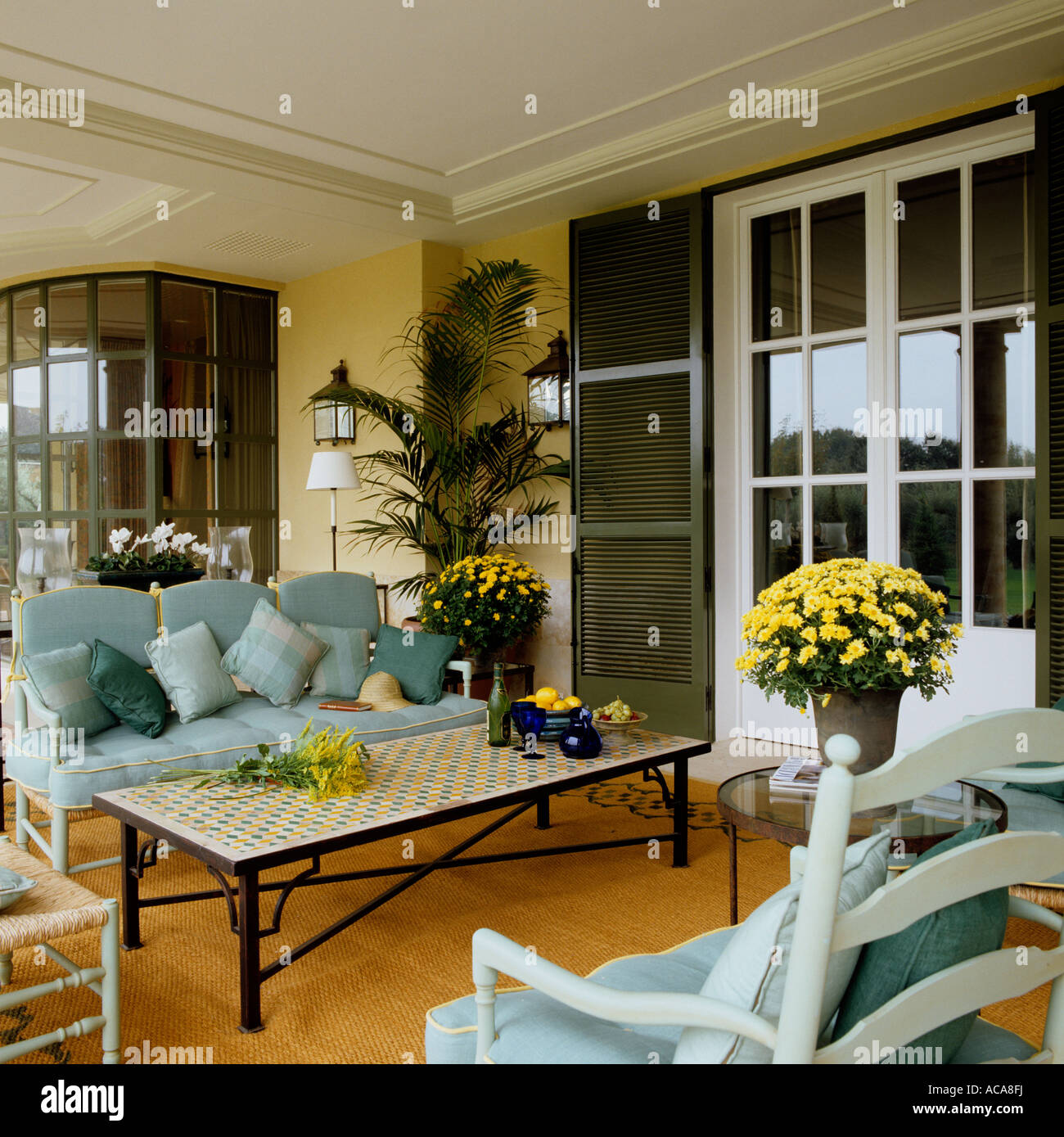 Veranda / summer room with blue upholstered sofa with yellow flower arrangement Stock Photo