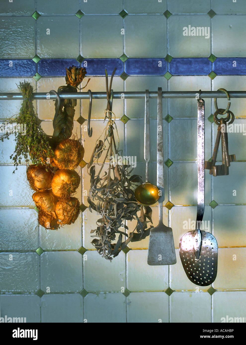 Tiled wall with garlic, dried sage and kitchenware, old keys Stock Photo