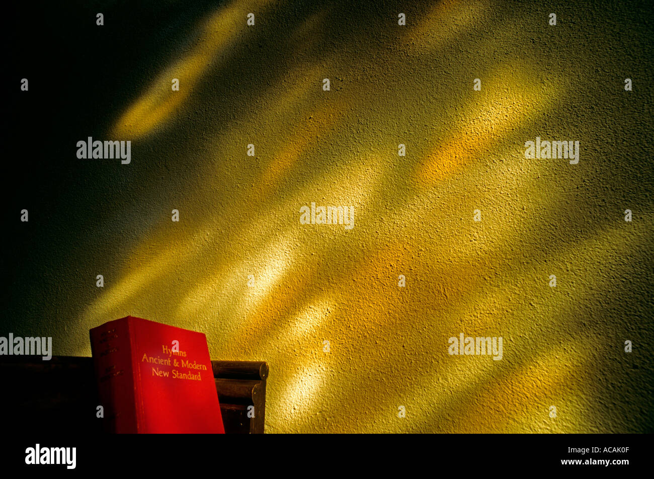 Hymn book on church pew with dappled light of stained glass window on church wall Stock Photo