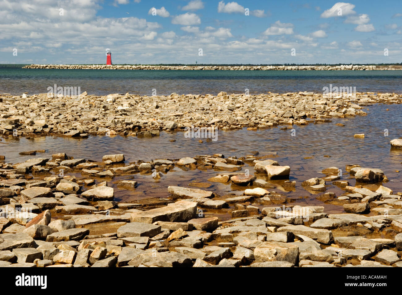 Rocks along Lake Michigan Shoreline with Manistique East Breakwater Lighthouse in the Background Manistique Michigan Stock Photo