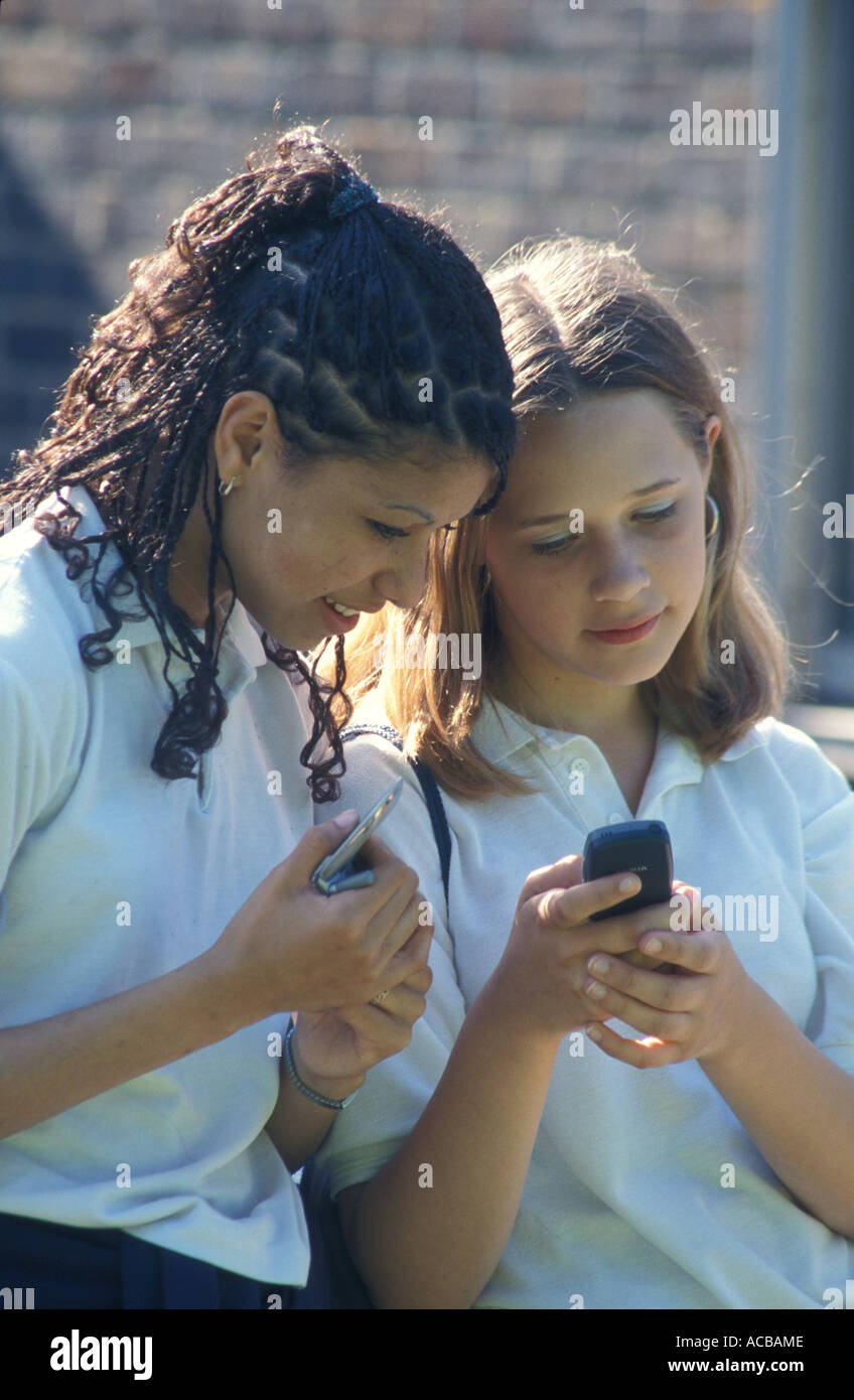 Two secondary school girls at school texting on mobile phones Stock Photo