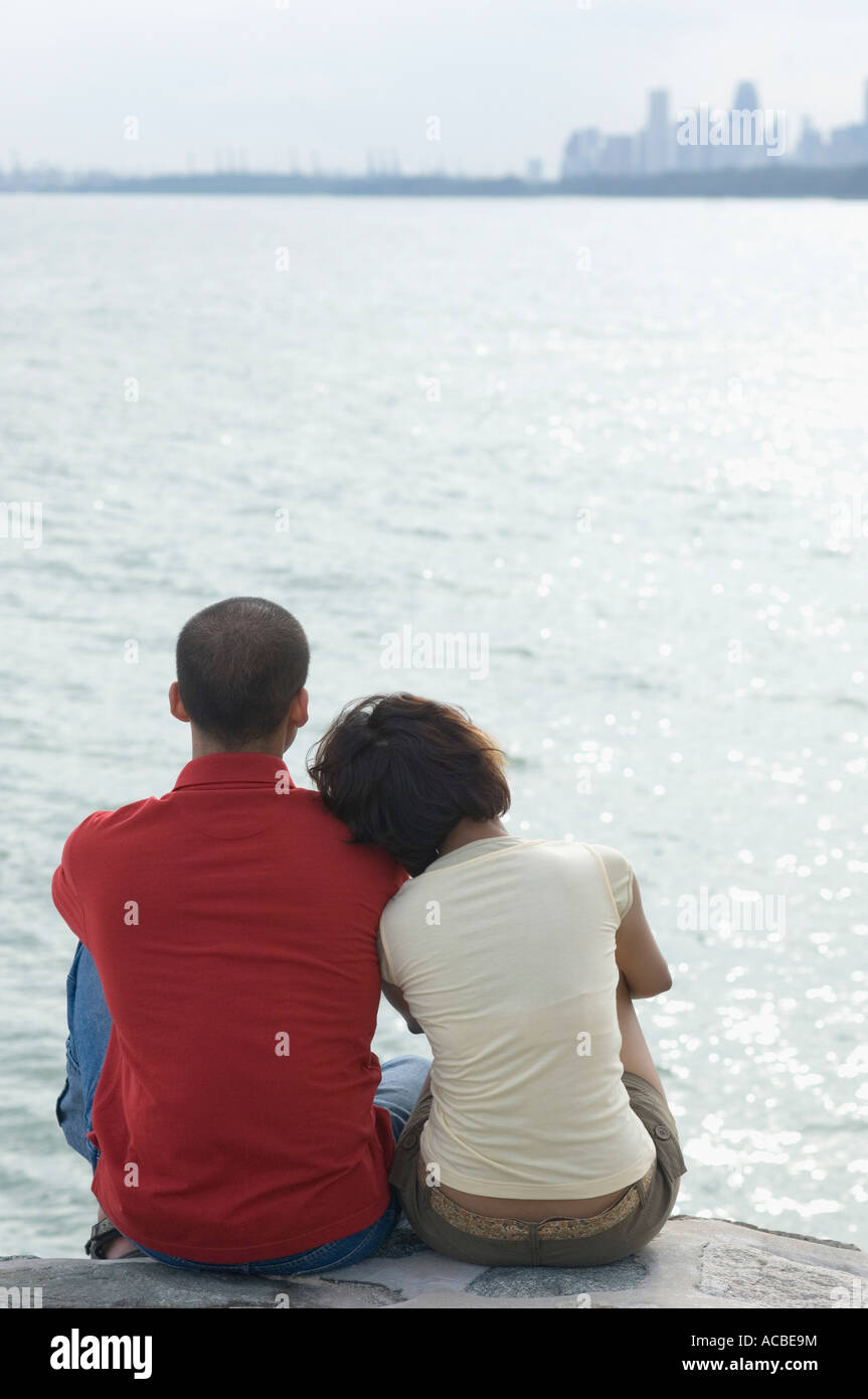 Rear view of a mid adult woman and a young man sitting on the beach ...