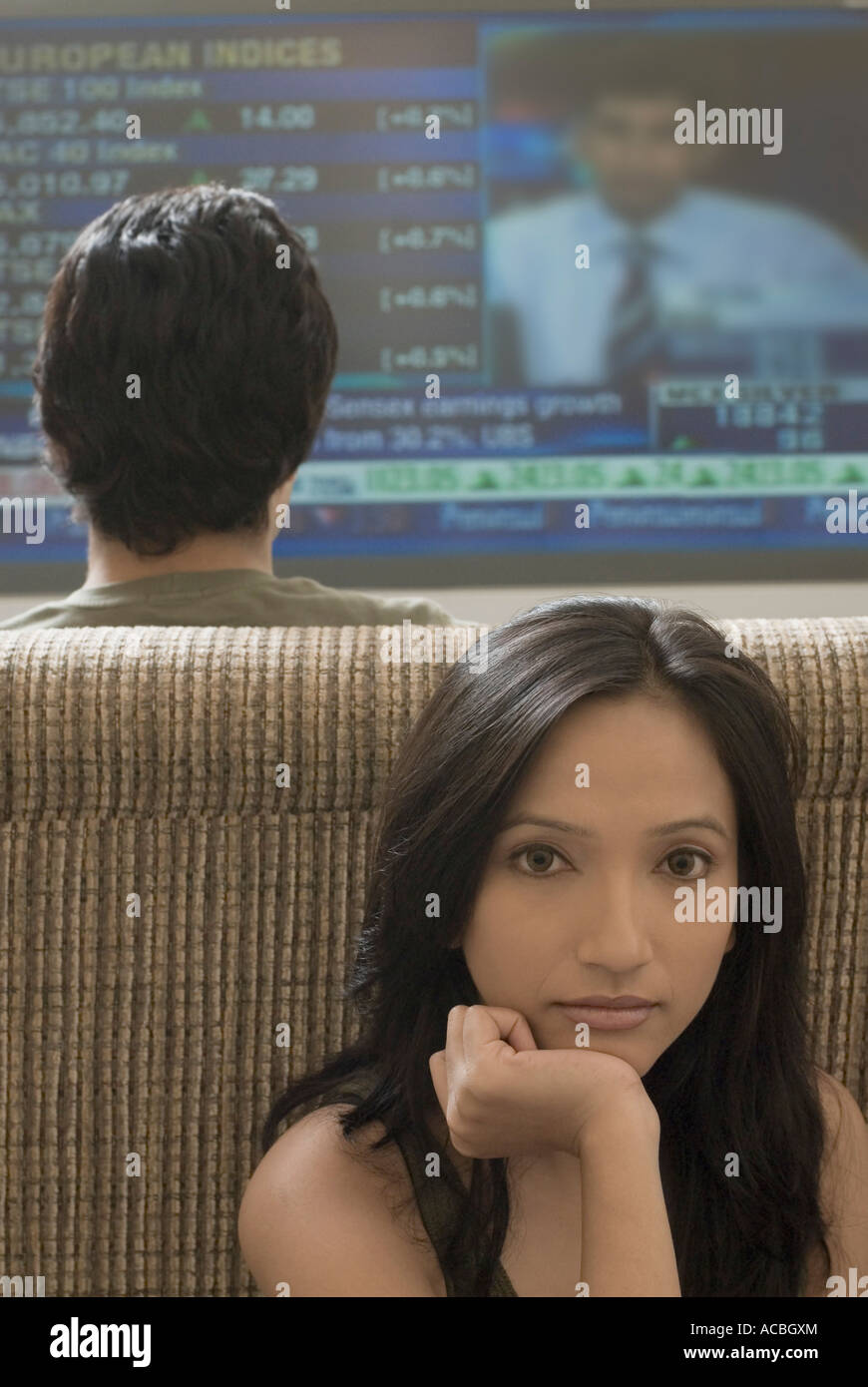Rear view of a young man watching television with a young woman sitting behind him Stock Photo