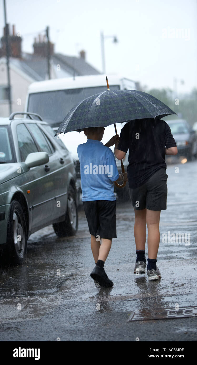 Two school children sheltering from the rain under an umbrella Stock Photo