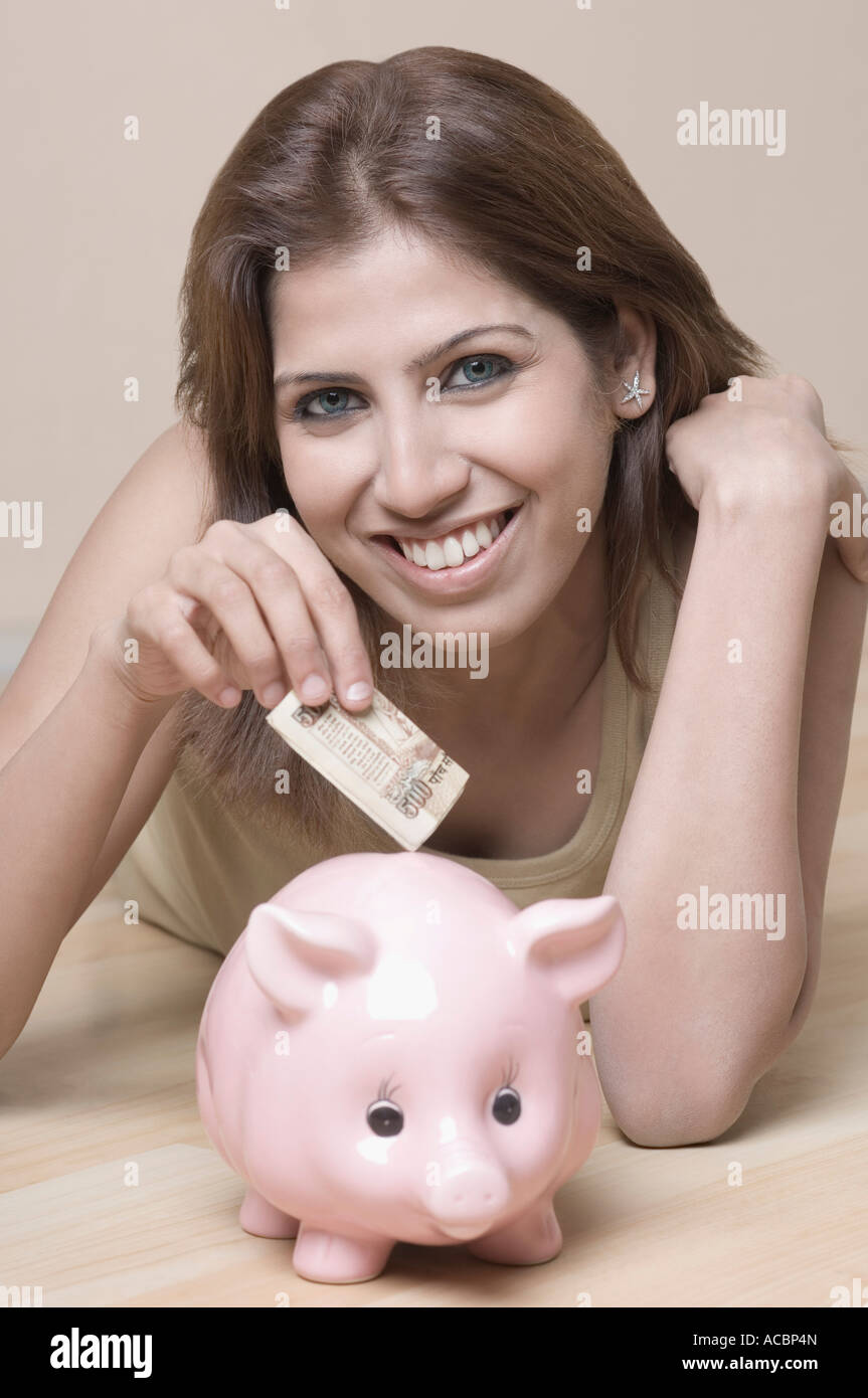 Portrait of a young woman putting money in a piggy bank Stock Photo - Alamy