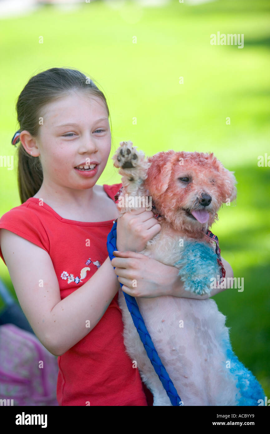 A small girl a parade holds a dog that is painted red white and blue for the 4th of july Stock Photo