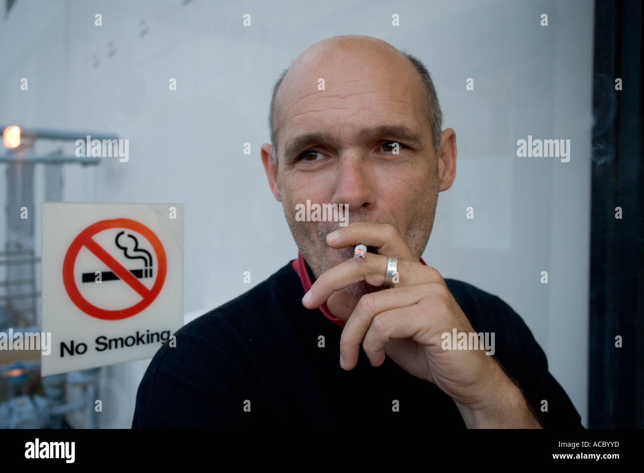 Man smoke in front of non smoking sign Stock Photo