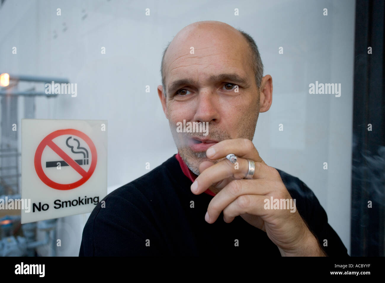Man smoke in front of non smoking sign Stock Photo