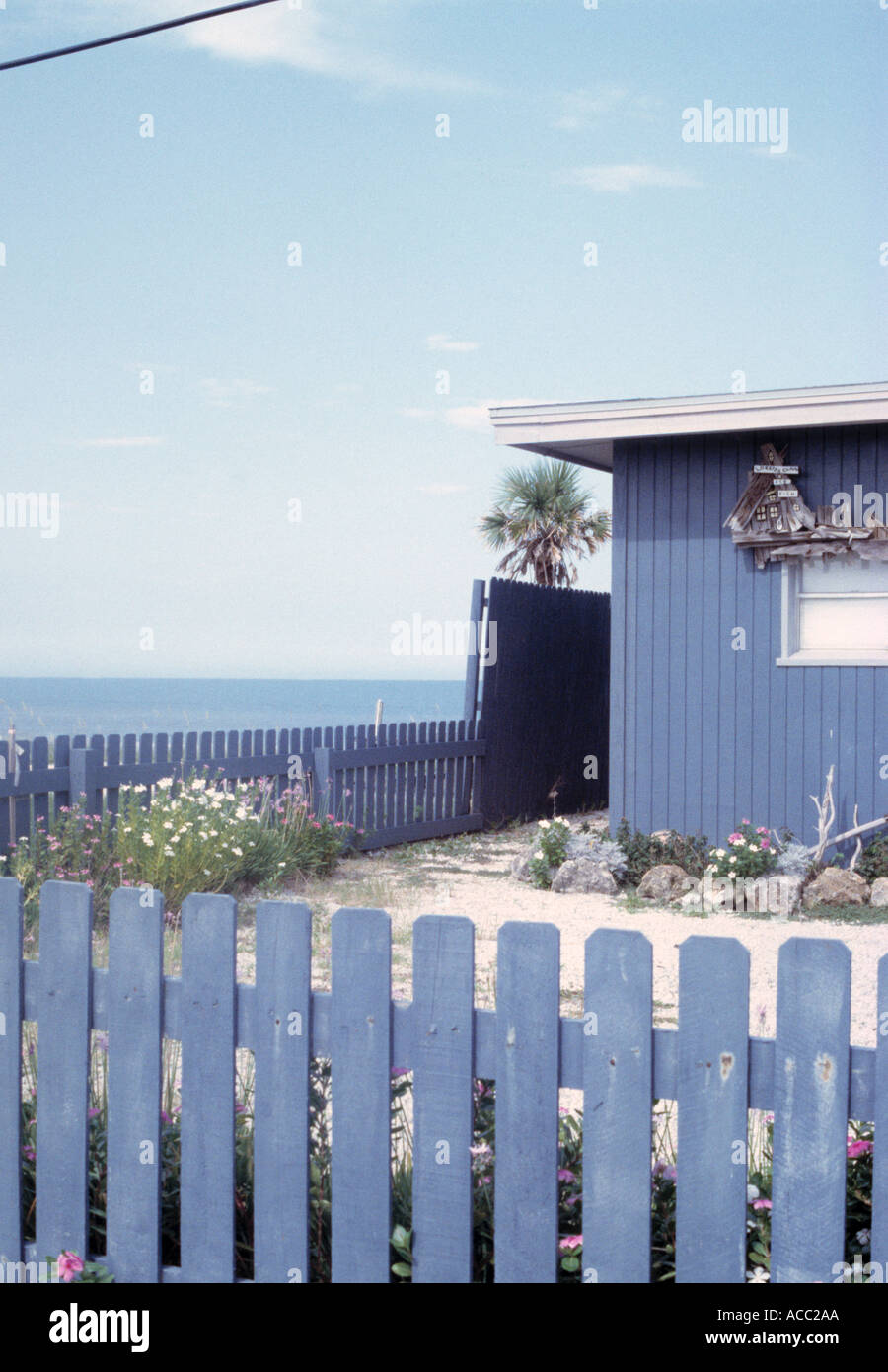 Blue picket fence surrounding garden of small blue beach house with