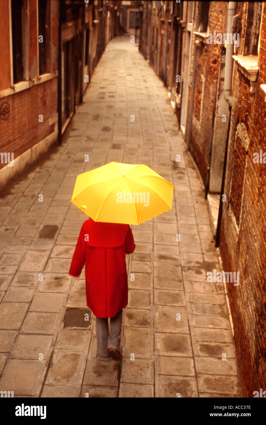 Girl in red rain coat and yellow umbrella walking on street in Venice Italy Stock Photo