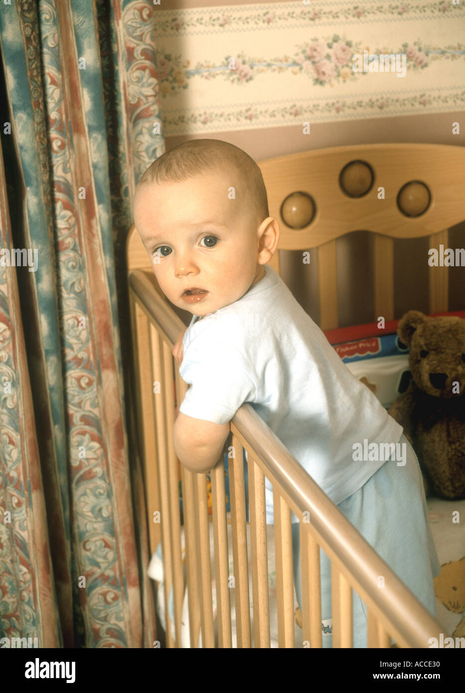 Baby boy leaning over a cot in his nursery Stock Photo