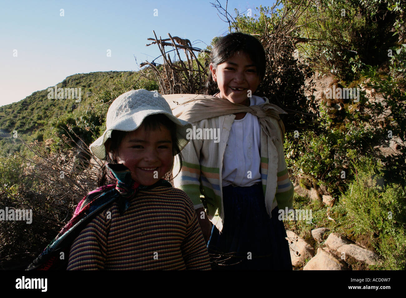 Small girls carrying woodfire walking down path on Isla del Sol, Sun Island, Lake Titicaca, Bolivia Stock Photo