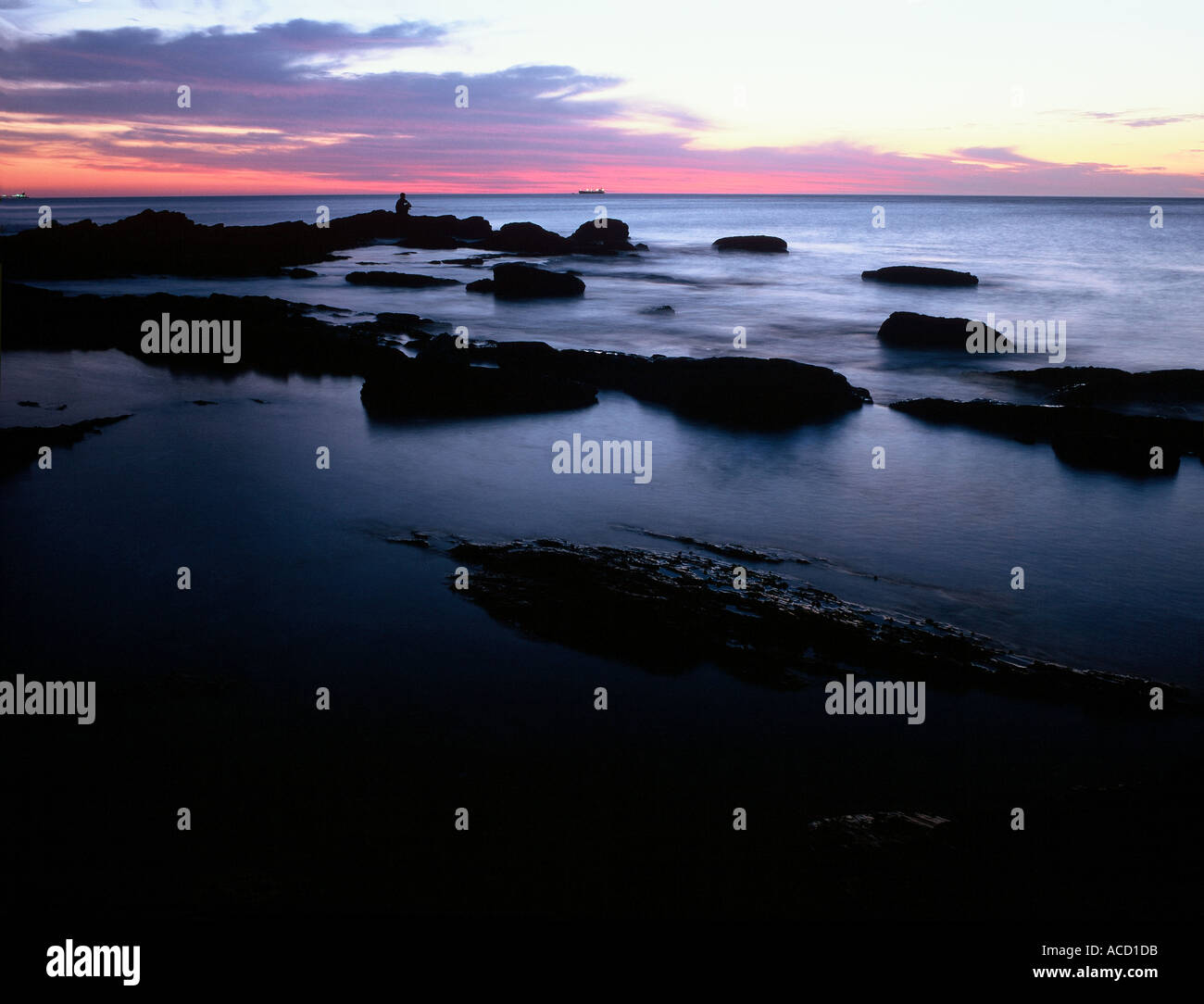 Lone angler sitting on rock at dusk Stock Photo - Alamy