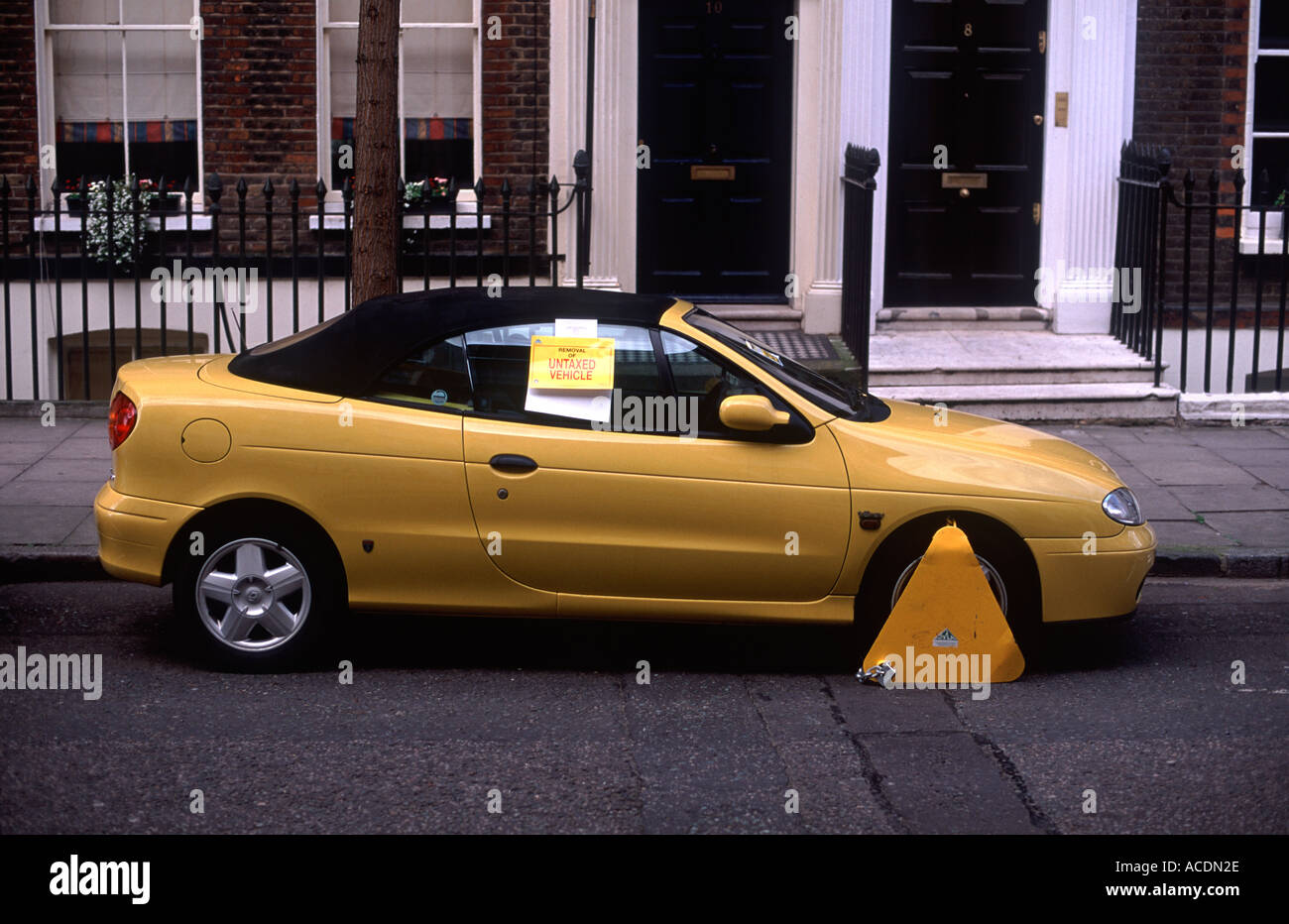 Yellow sports car clamped on residential street, Camden, London. Sign on car window reads: 'Removal of Untaxed Vehicle'. Stock Photo