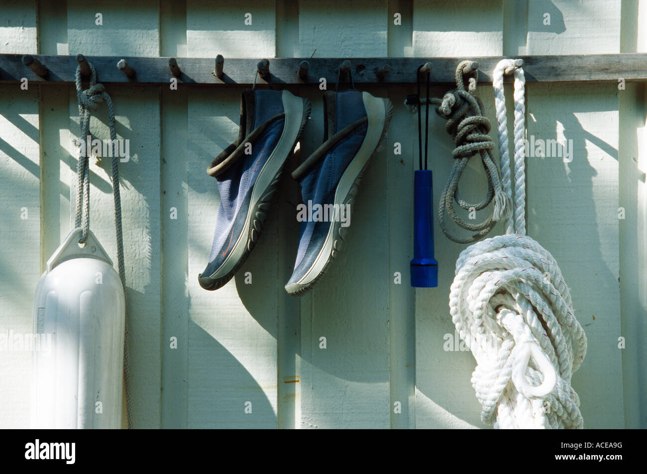 A pair of shoes a buoy and ropes hanging on hooks on a house wall. Stock Photo