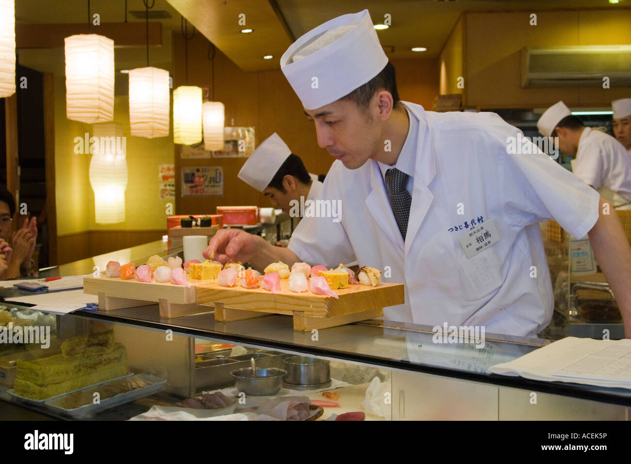Sushi chef preparing sushi and putting them on wooden geta trays at the counter of a Japanese sushi restaurant Tokyo Japan Stock Photo