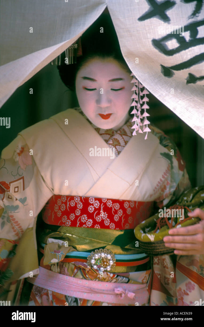 Maiko or geisha apprentice exits through a doorway noren curtain Stock Photo
