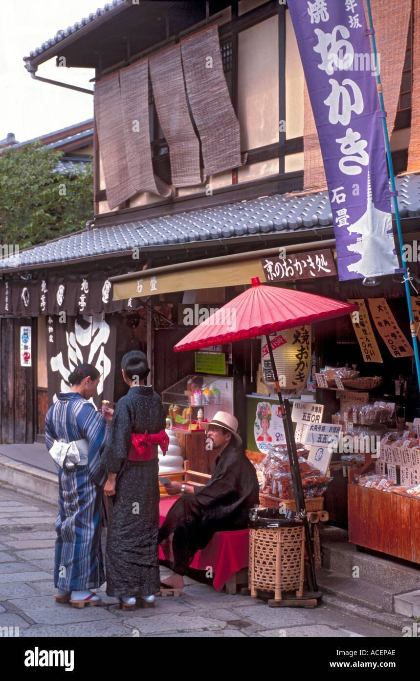 Tourists wearing summer yukata stop to chat with man resting on bench in the historical district of Kyoto Stock Photo