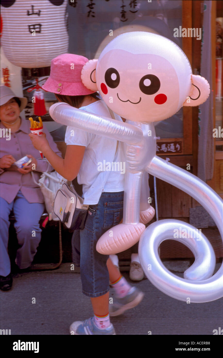 Girl at festival carrying inflatable toy monkey on her back Stock Photo