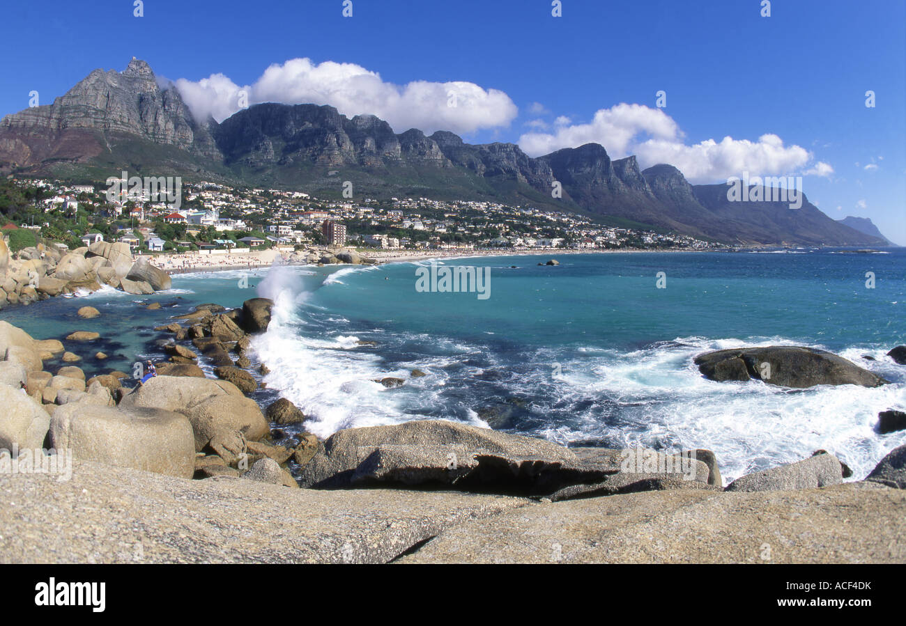 A wave washing up on the rocks at Camps Bay against the backdrop of the with twelve apostles. Stock Photo
