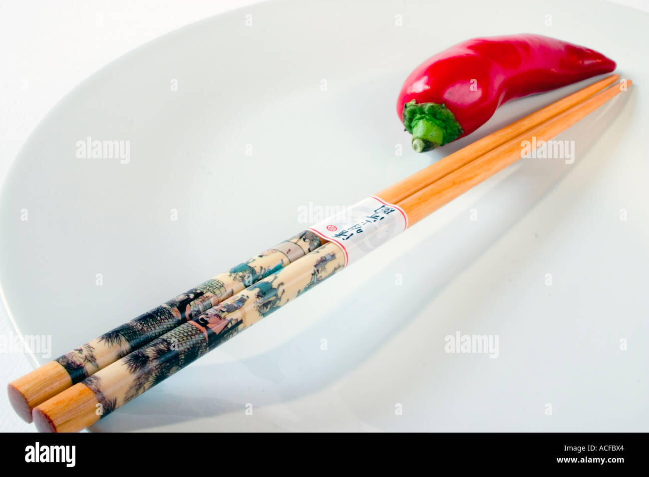 Single red chilli pepper on a white plate with a pair of chopsticks Stock Photo