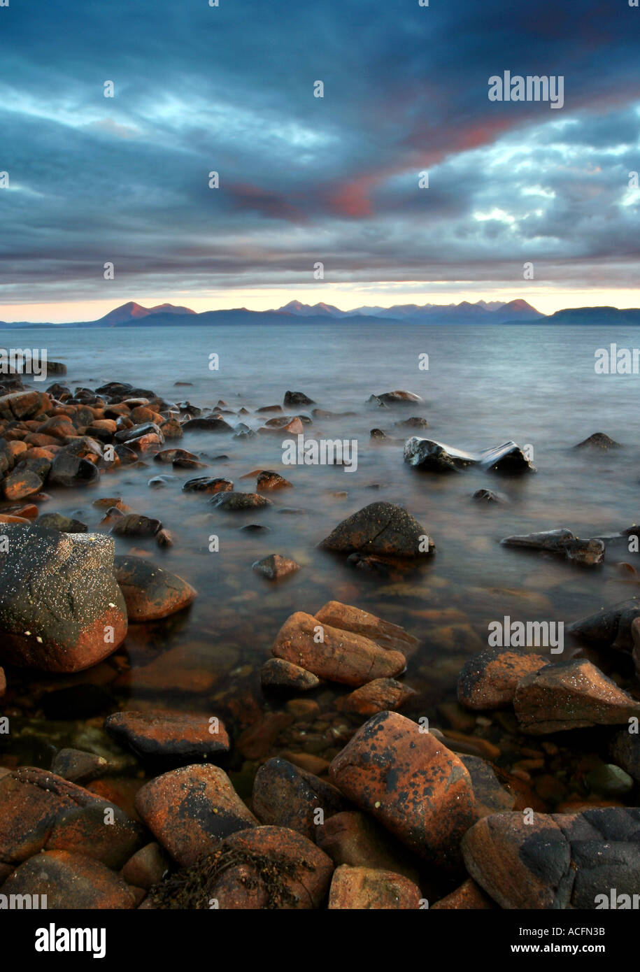The Cuillin mountain range in soft dusk light from Applecross bay with crustacean covered rocks in the foreground Stock Photo
