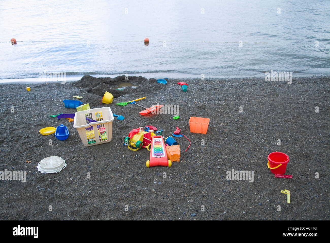 Children's beach toys spread over sand at edge of water. Stock Photo