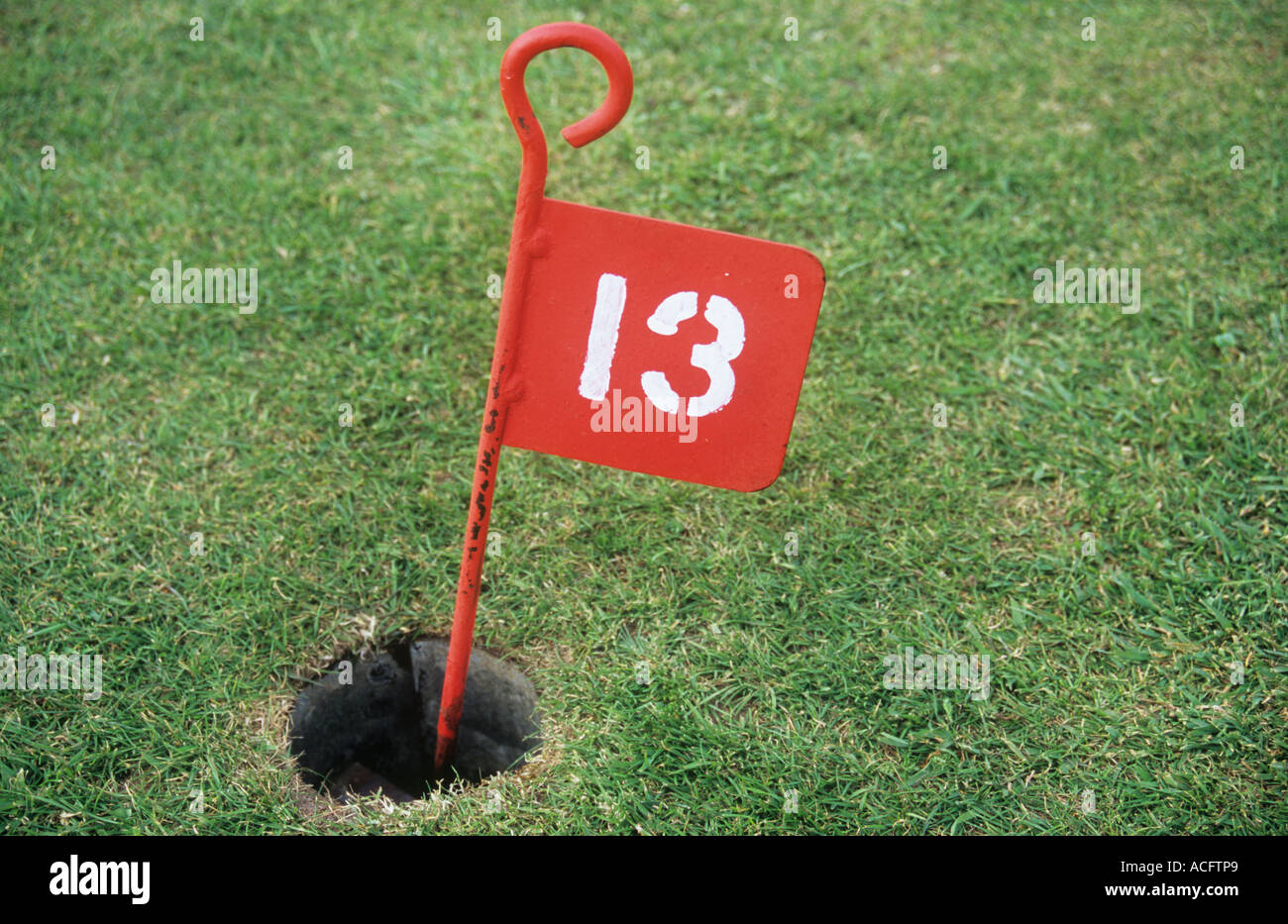 Close up of a red marker sign with a white stencilled 13 in the hole of a golf pitch and putt green Stock Photo