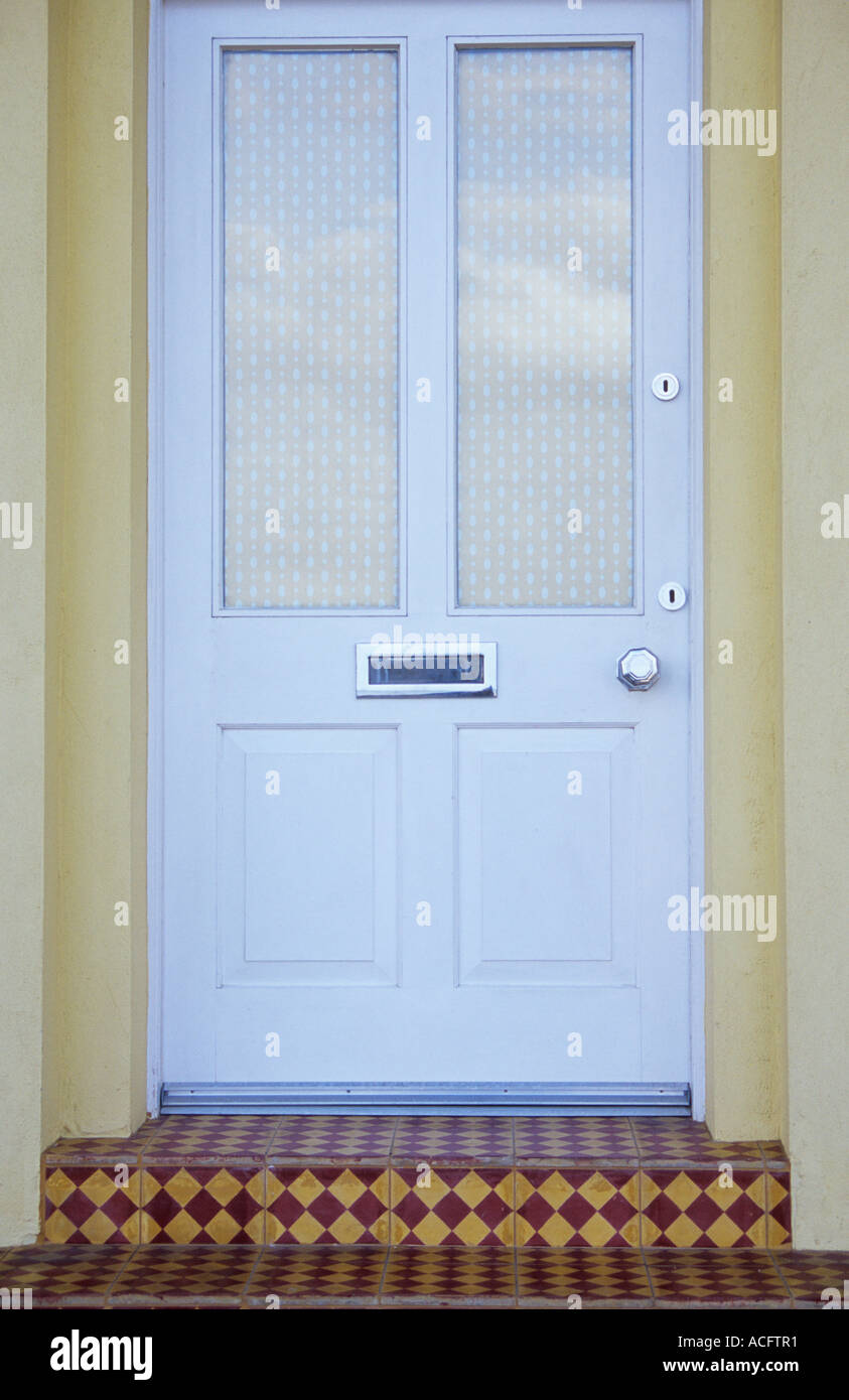 Detail of modern windowed and panelled white front door with blind letterbox handle and draughtproofing and diamond tiled steps Stock Photo