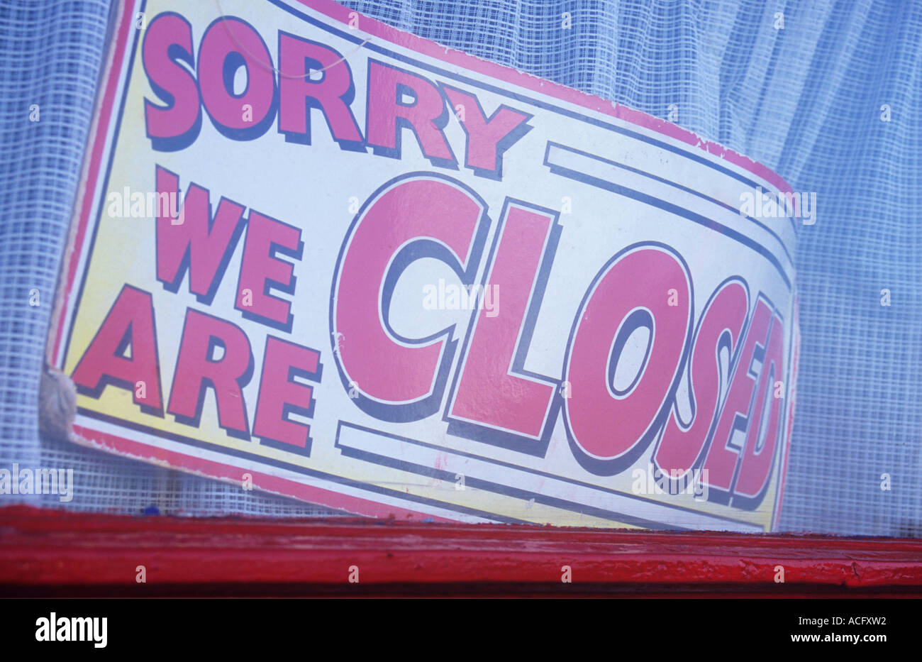 Close up of faded and curled red and yellow sign in a shop or kiosk or cafe window with net curtain stating Sorry We are closed Stock Photo