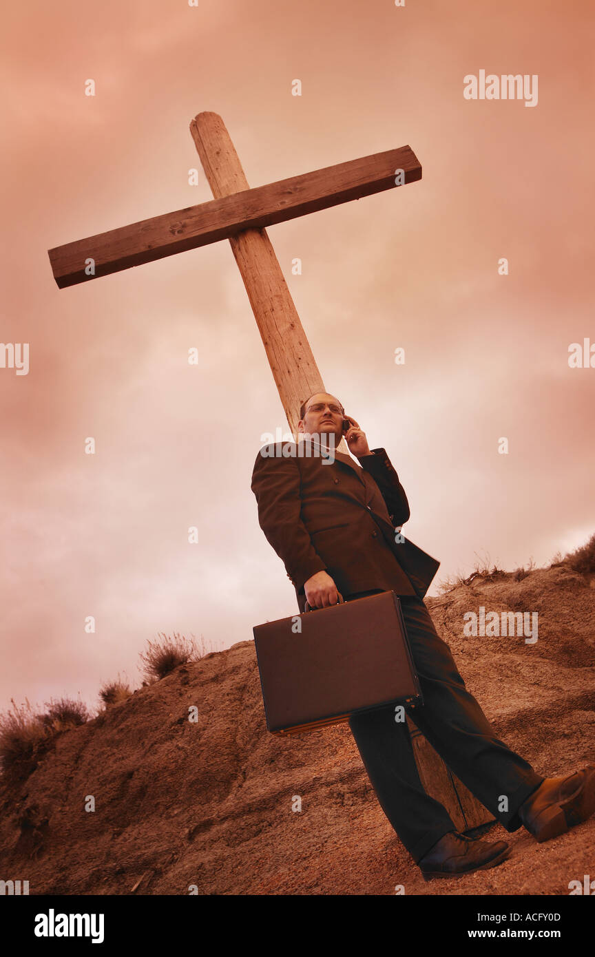 Businessman on phone leaning on a cross Stock Photo