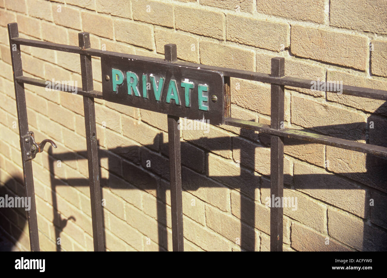 Detail of plain metal gate with sign stating Private and casting a deep shadow on a plain pale brickwall Stock Photo