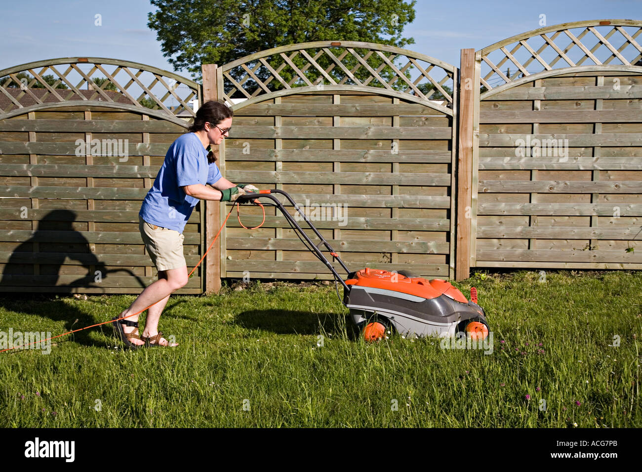 Woman wearing gardening gloves mowing lawn with electric mower Wales UK Stock Photo