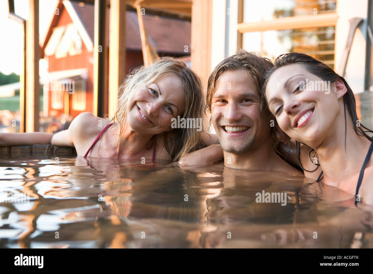 Two women and a man bathing in a barrel outdoors. Stock Photo