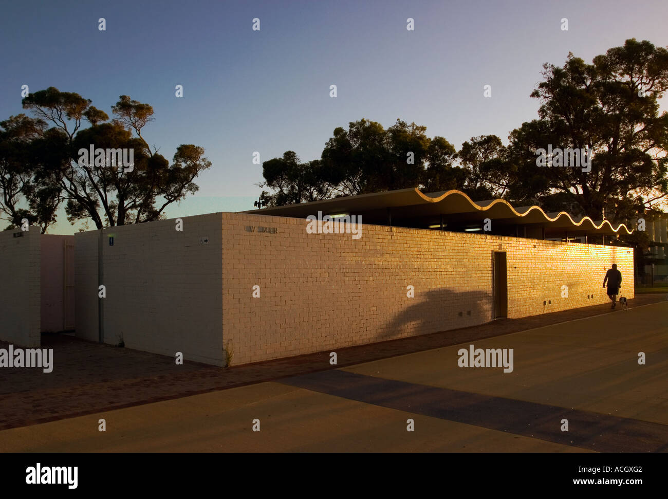 Man walks dog past public toilet at dusk Rockingham Western Australia Stock Photo